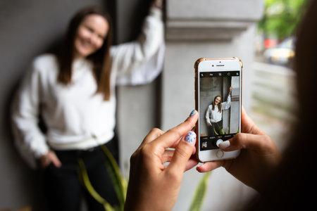 Two young women take photos and videos of each other on smartphone on a terraceの写真素材