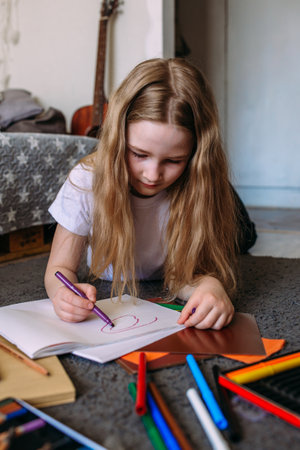 The girl after school plays at home, draws with pencils and felt-tip pens