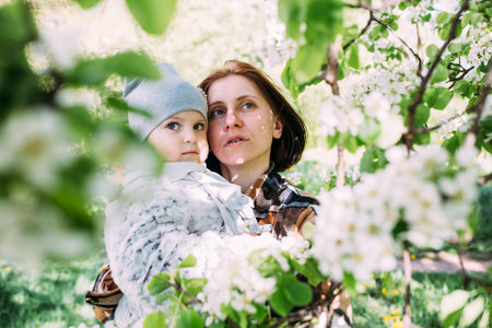 Young woman with her daughter in nature admires white flowering of spring treesの写真素材