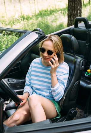A woman is driving a convertible car. Summer road trip to natureの写真素材