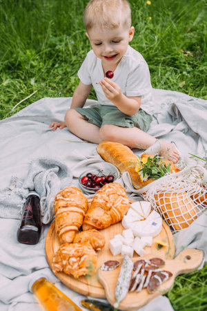 Boy child preschooler on a picnic. Smiles, eating cherries and enjoying summer.の写真素材