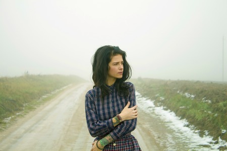 Attractive, single, hipster girl frozen country road in fog