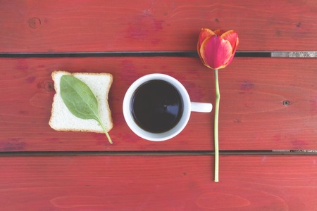 Composition tulip in a cup of coffee, a sandwich with fresh leaf lettuce on a red wooden surfaceの写真素材