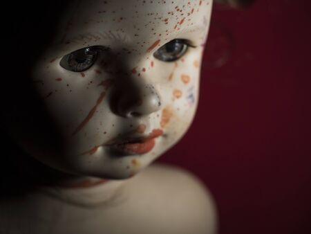 close-up of blood-stained doll face in twilight on red background close-upの写真素材
