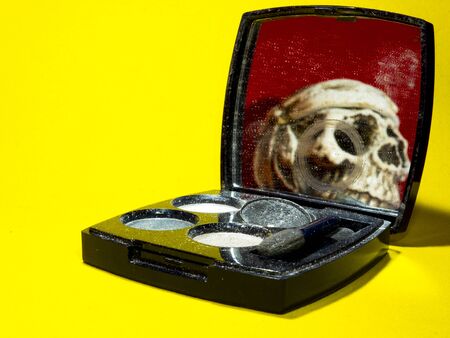 old dusty female palette on a yellow background in the mirror of which a human skull is reflected on a red background. still life close-upの写真素材