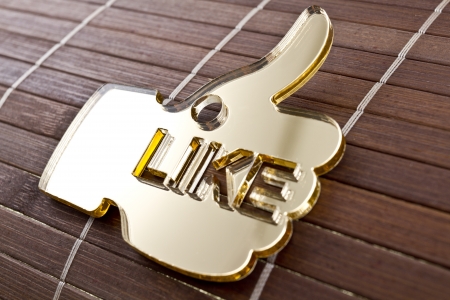Golden thumb up shape made of plexiglas on a wood background の写真素材