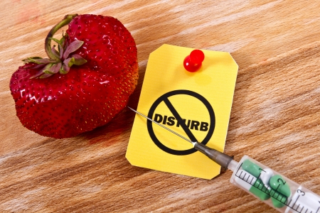 Stop GMO concept shot. Genetic food engineering concept with a fresh red strawberry on a wooden background, syringe with capsules and の写真素材