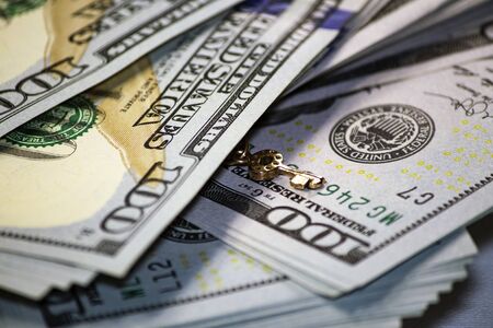 Little golden key on background of a stack of one hundred dollar bills. A little key for a big financial success business concept.の写真素材