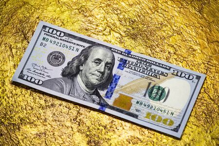 One hundred dollar banknote on a gold close-up. Dollar versus gold concept.の写真素材
