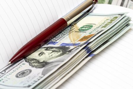 Close up of an empty business notepad and a pen with a pile of US dollarsの写真素材