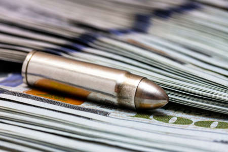 Gun bullet laying on a stack of american dollars. Ammunition from the gun on money bills close up.