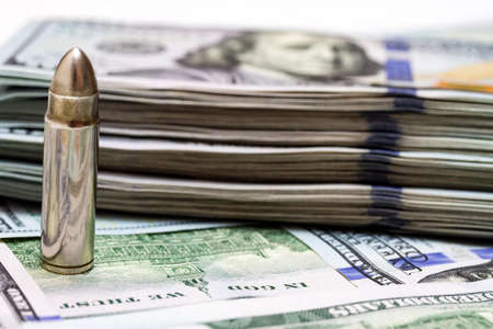 Realistic gun bullet stands against the background of a stack of usd money.