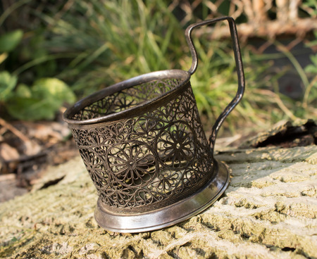 patterned silver stand for glasses,slightly covered with patina, stands on a piece of bark from the tree, near the grass, Sunny day,a little bit bentの写真素材