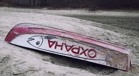 Old Upturned Boat red Color Lies on the Shore of the Dried Lake. The inscription on the side of the boat PROTECTIONの写真素材
