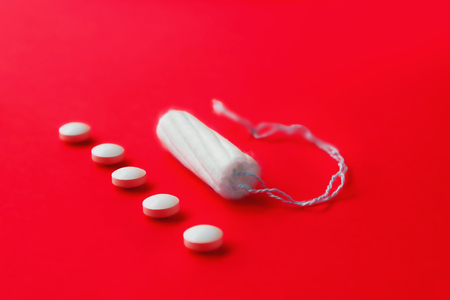 Tampon and female pain pills during menstruation on a red background. Protection from unwanted pregnancy, ovulationの写真素材