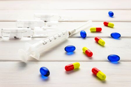 Prevention of influenza. The vaccine syringe and the bright capsules pills on a wooden white...
