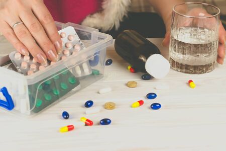 Close-up of bright colored medical pills and capsules with medicines and a glass of water next to...