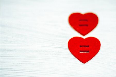 Two red hearts made of felt vertically one above the other on a white wooden background. Valentine's...