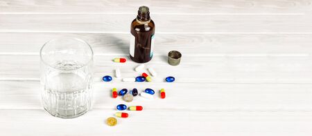 Close-up of bright colored medical tablets, a bottle of medicine and capsules with medicines and a glass of water. Scattered on the table Pills from the first-aid kit box.の写真素材