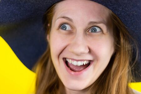 Close-up Portrait of a young beautiful red-haired girl smiling broadly and looking playfully to the side. on his head is a blue hat. On a yellow background .の写真素材