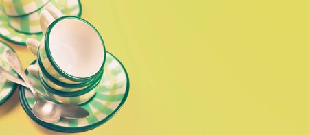 Beautiful little green striped two tea coffee cups and saucers spoons on a yellow background. The concept of home tea drinking, comfort. Banner, tinting.の写真素材
