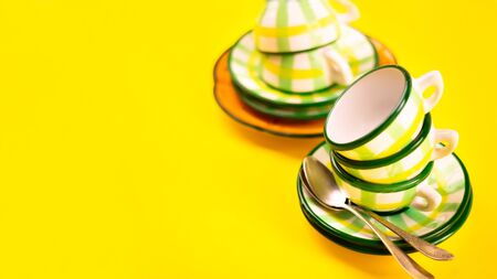 Beautiful little green striped two tea coffee cups stacked one in one and saucers and spoons on a yellow background. The concept of home tea drink. Bannerの写真素材