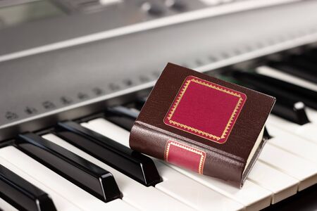 Close-up on the piano keys is a small decorative book. Playing by notes. Concept of romance and...