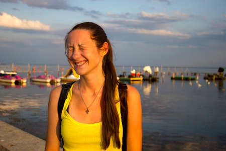 The happy girl closed her eyes with pleasure in the setting sun. Long hair and a smile on his face. In the background, the sea and water catamarans. The concept of happiness. Toned.の写真素材