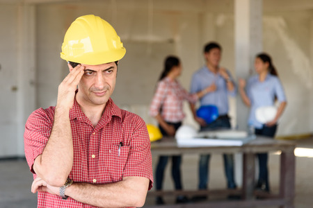Engineer leader headaches with blurred of diverse engineers discussing about project in backgroundの写真素材