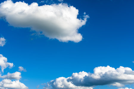 Minimalist scene of white fluffy clouds against a deep blue sky, capturing the beauty and tranquility of nature.の写真素材