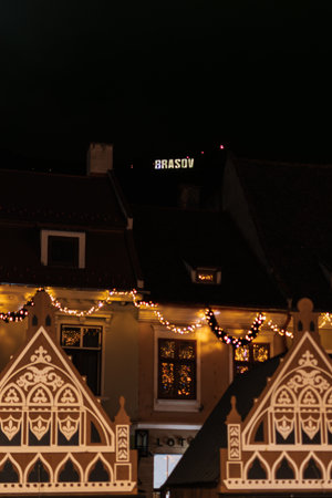 Vertical shot of wooden Christmas market stalls and rooftops in Brasov at night. The illuminated...