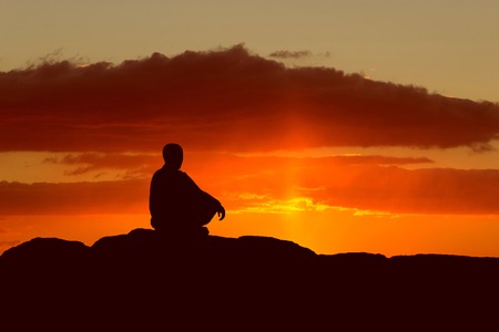 buddhist monk meditating at sunset sitting on a rock by the seaの写真素材