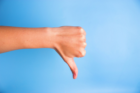 Closeup of woman's hand gesturing thumbs down against blue background