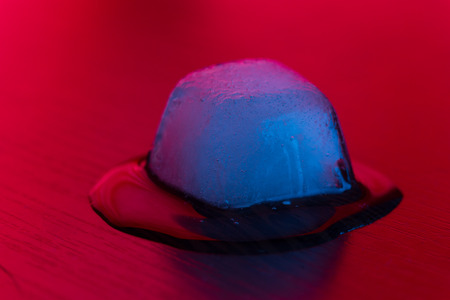 Melting ice cube close up in neon lightの写真素材
