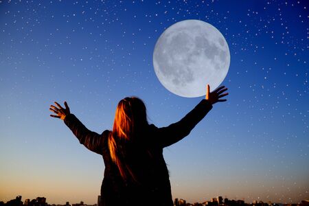 Woman with rased hand over night sky backgroundの写真素材