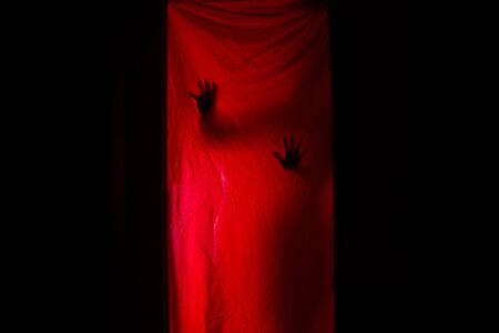 Silhouette of a woman behind red curtains. Horror