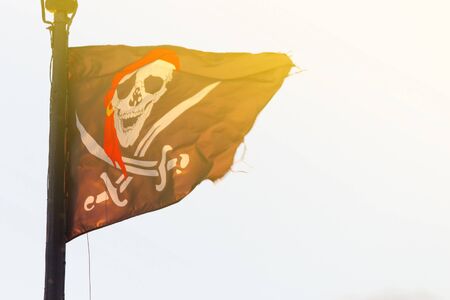 Pirate flag on ship over sky background. backlit.