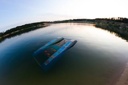 Sinking catamaran in lake. Old blue catamaran
