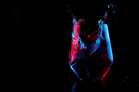 Water highlighted in blue and red splashing into a glass goblet on a black backgroundの写真素材