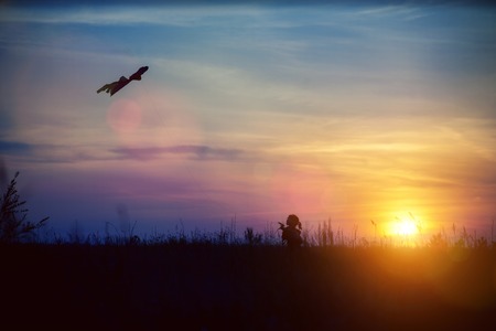 silhouette of a girl who plays a kite at sunsetの写真素材