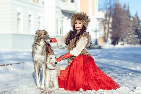 The girl in a fur vest and red dress walking with dogの写真素材