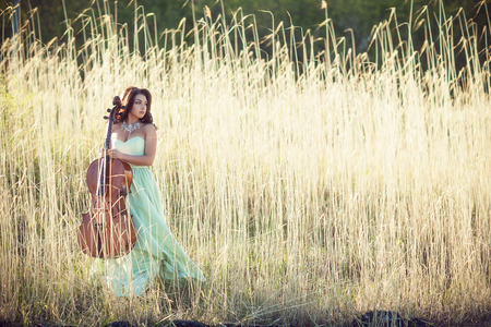 Girl with a cello in a tall grassの写真素材