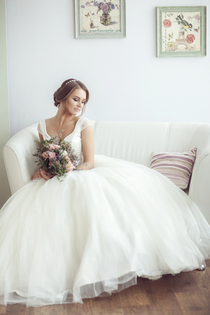 Portrait of a bride with a bouquet in a bright room on a white sofaの写真素材