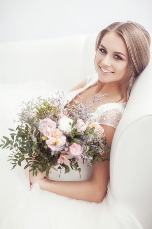 Portrait of a bride with a bouquet in a bright room on a white sofaの写真素材