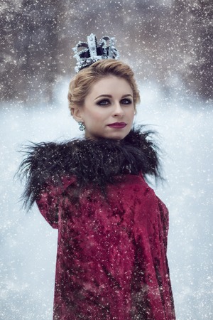 Portrait of a beautiful blonde in a red cloak and a small crownの写真素材
