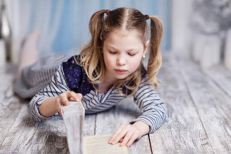 A girl is reading a white book lying on the floorの写真素材