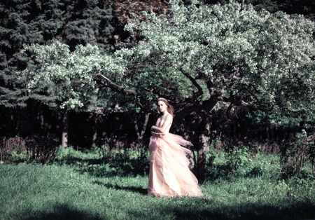 Lovely young girl in pink dress in a flower gardenの写真素材