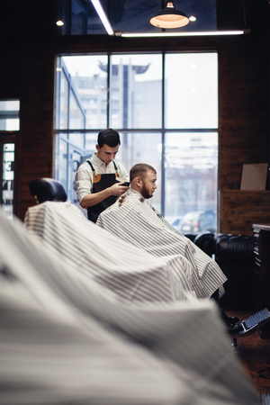Salon barbershop. Barber and client in the chair against the windowの写真素材