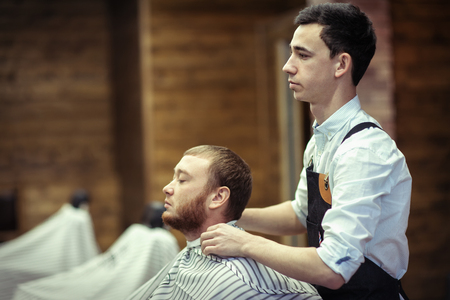 Barber with a client in a hair salon on a wooden wall backgroundの写真素材