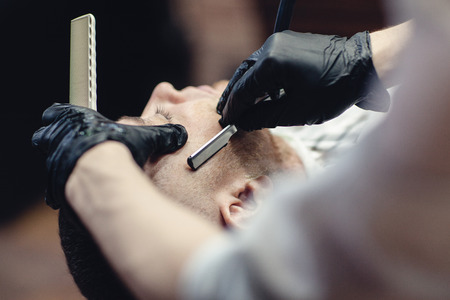 Hairdresser in black gloves shaves the razor's beard of the client